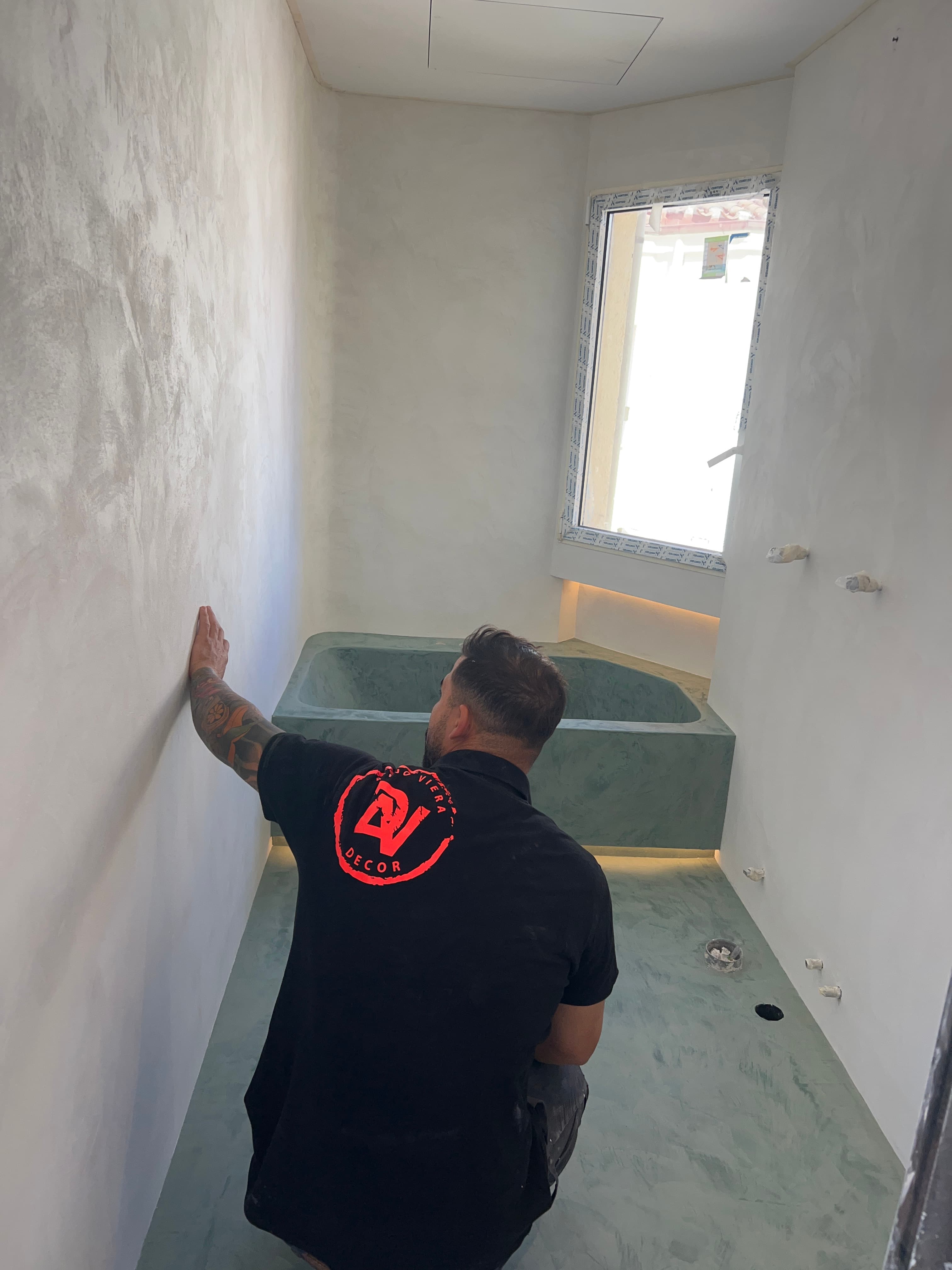 Alejo Viera con la camiseta de su marca, trabajando en una obra con paredes en microcemento verde grisáceo recién aplicado
