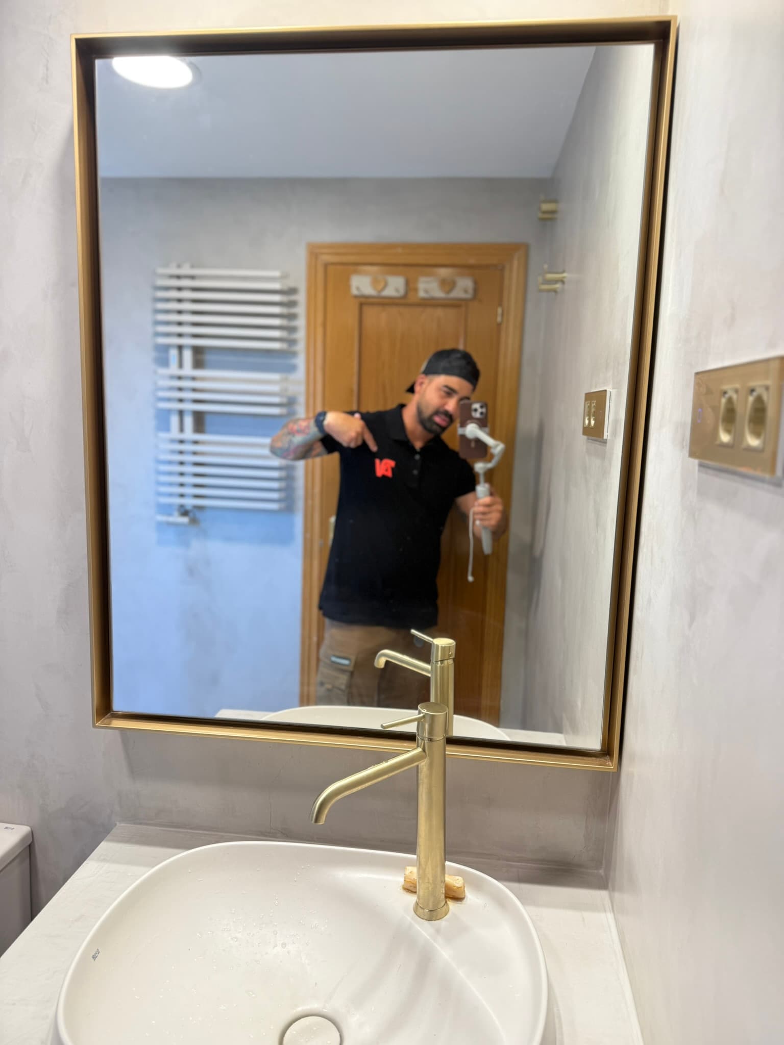 Alejo Viera fotografiado frente al espejo de un baño en microcemento recién terminado, con grifería y marco de espejo en dorado