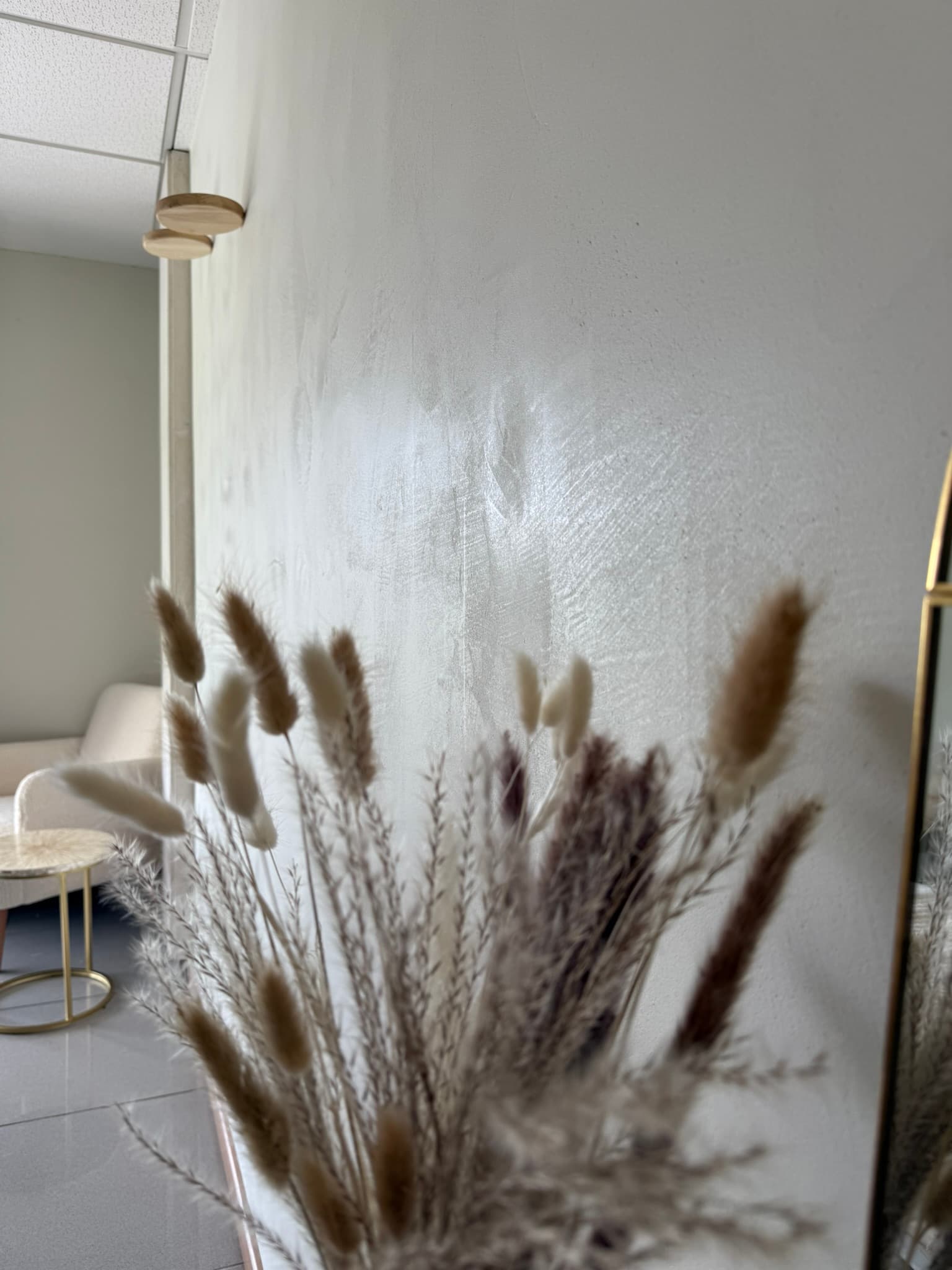 Textura de estuco veneciano blanco aplicada a la pared de un salón, junto a un jarrón con ramas secas y un sofá tapizado en beige