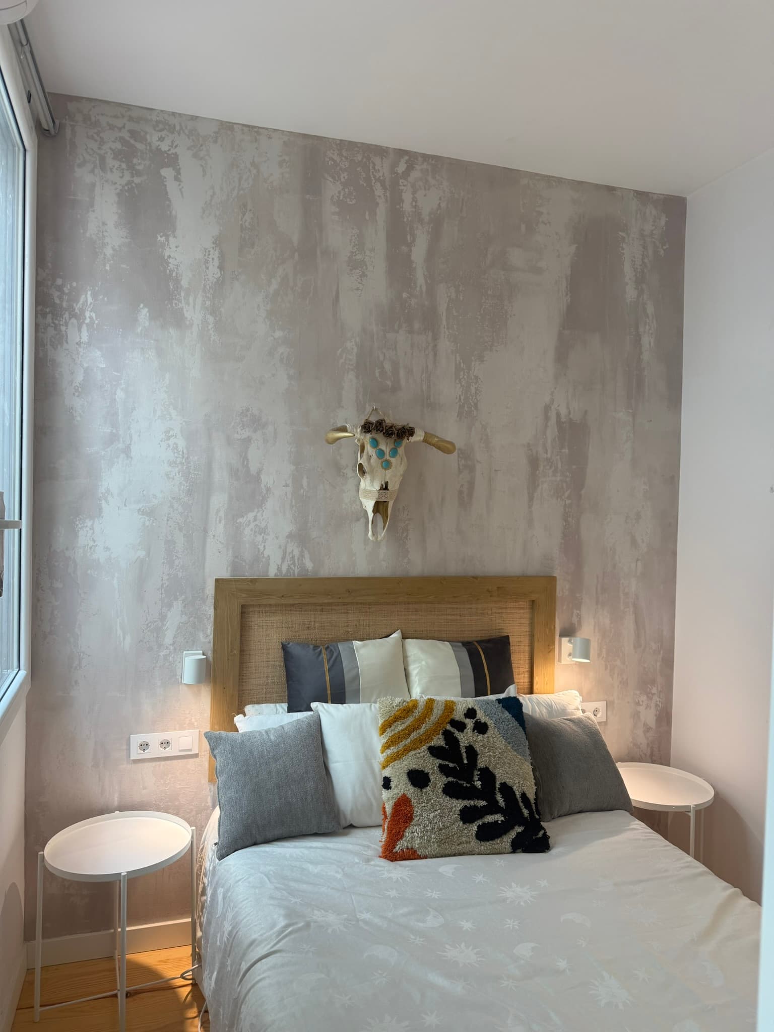 Cabecero de dormitorio con pared en estuco gris veteado y una calavera de vaca decorativa con cuentas turquesa como elemento central