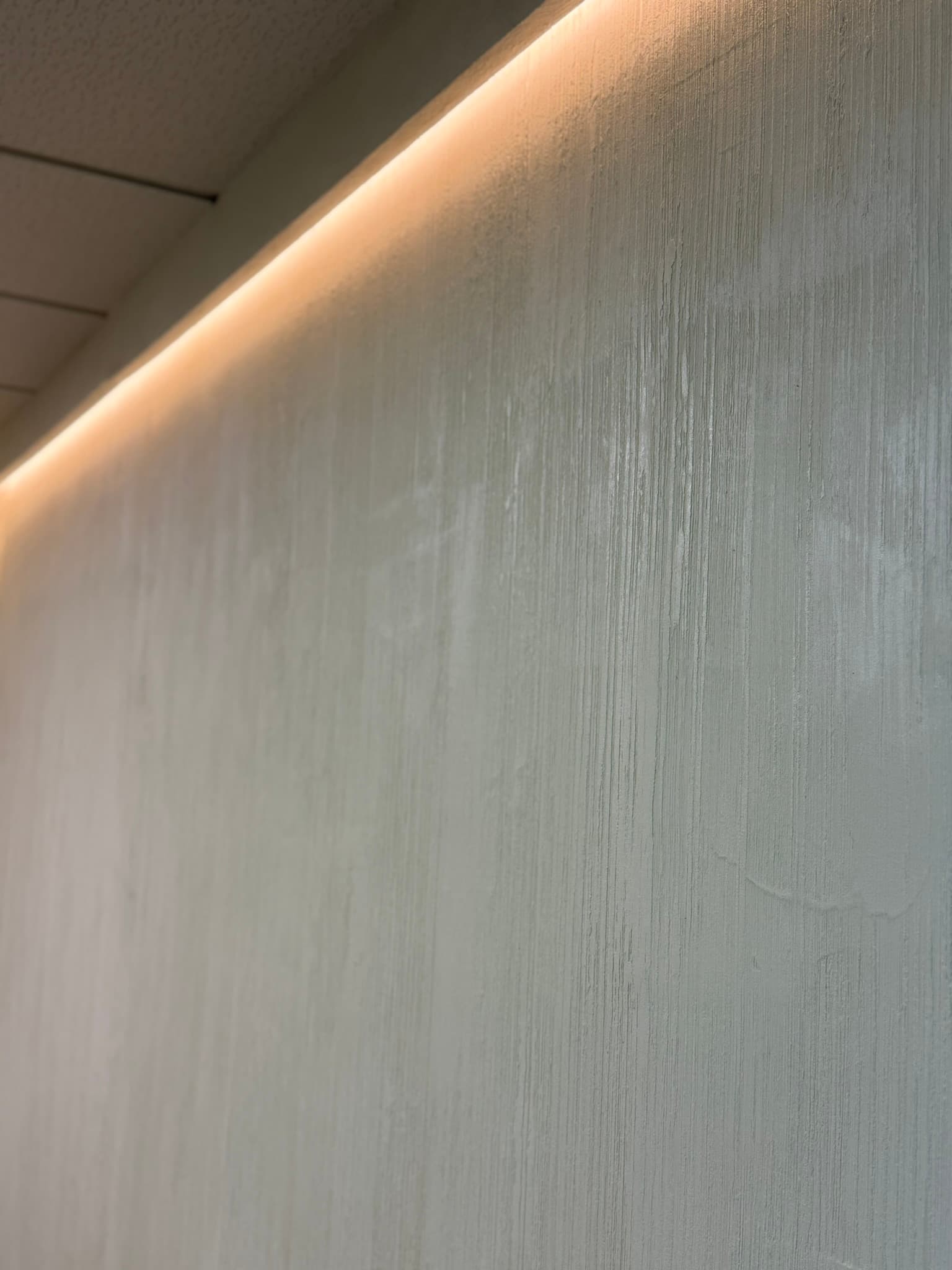 Detalle de estuco texturizado en tono crema con veta vertical marcada, realzado por iluminación LED indirecta bajo techo