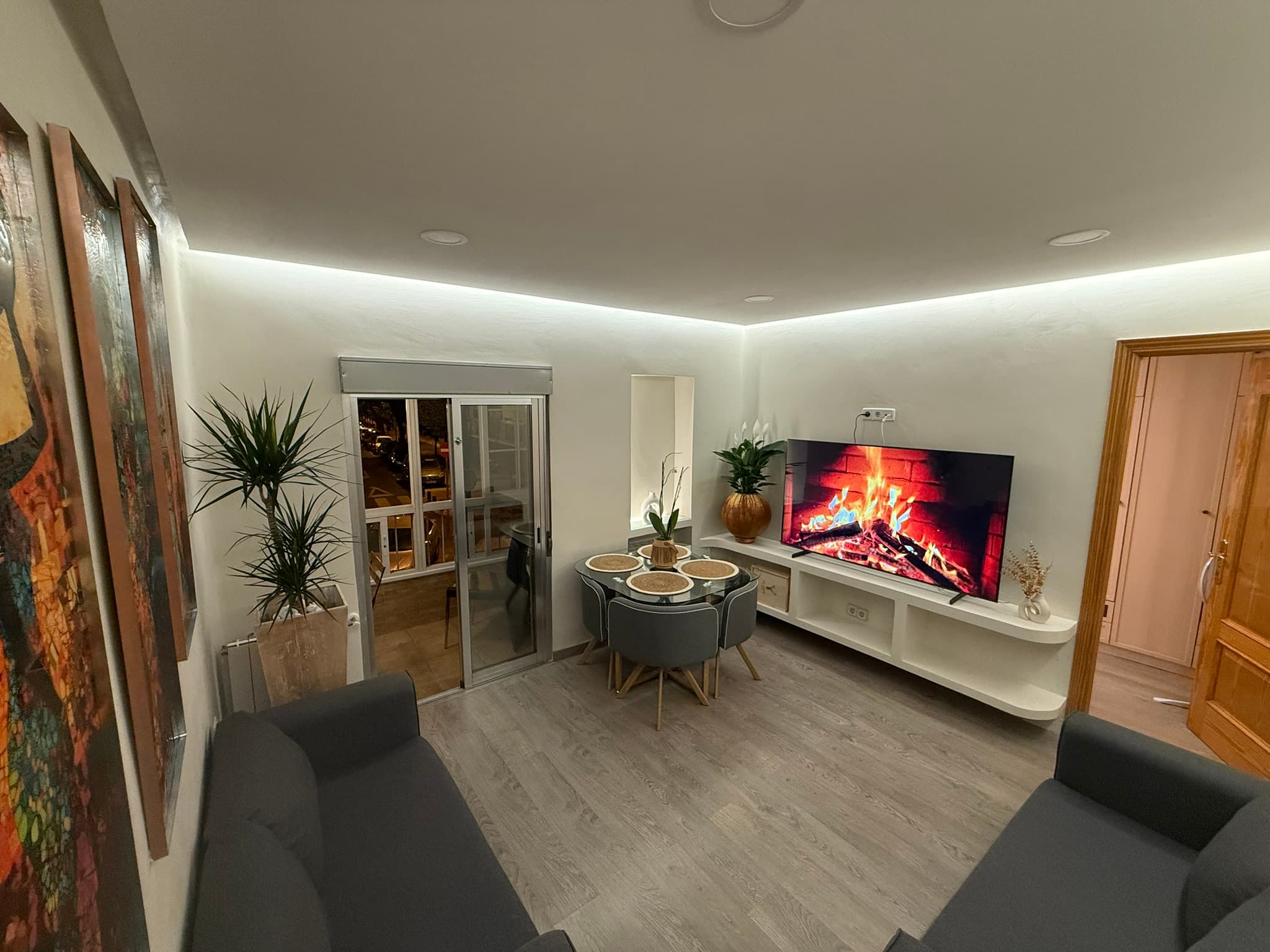 Salón reformado con paredes en estuco blanco liso, mueble de televisión a medida e iluminación indirecta perimetral en el techo