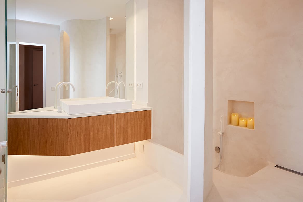 Detalle de pared curva en microcemento crema con hornacina portavelas integrada, junto a la ducha