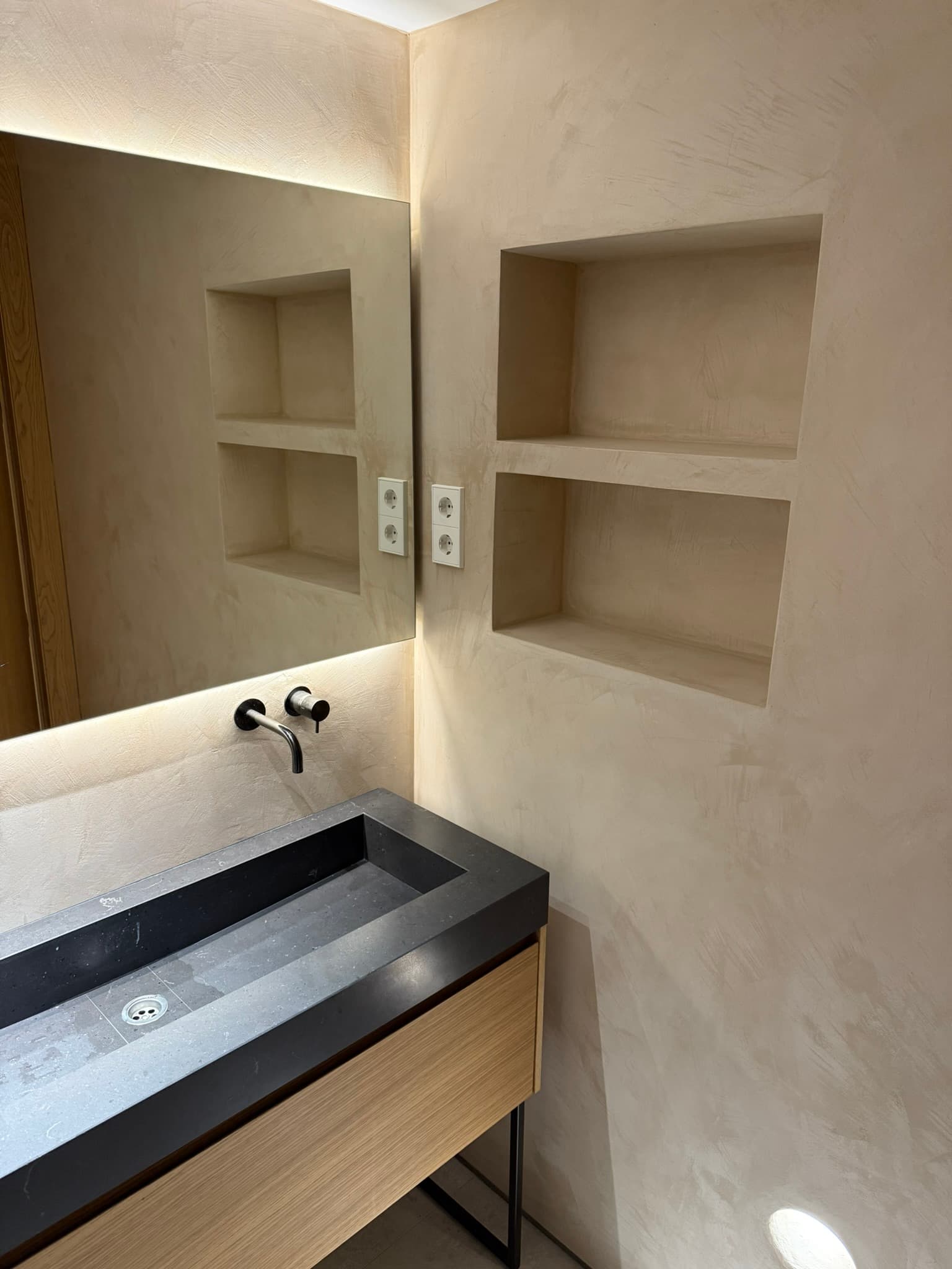 Aseo en microcemento crema con lavabo cilíndrico exento, inodoro suspendido y ventana circular