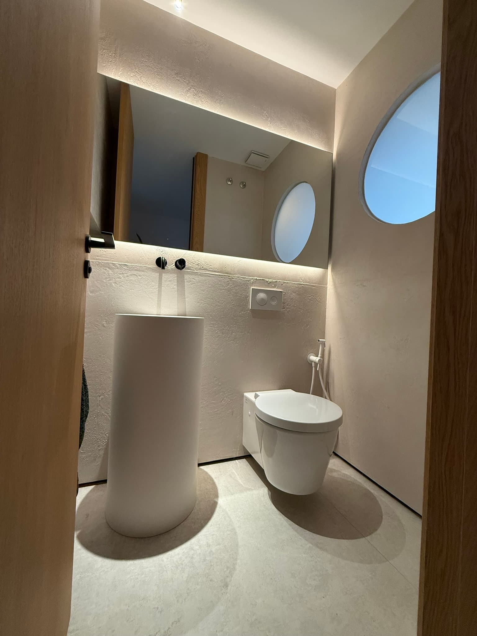 Bañera integrada de obra acabada en microcemento verde grisáceo, junto a una ventana con reja de forja