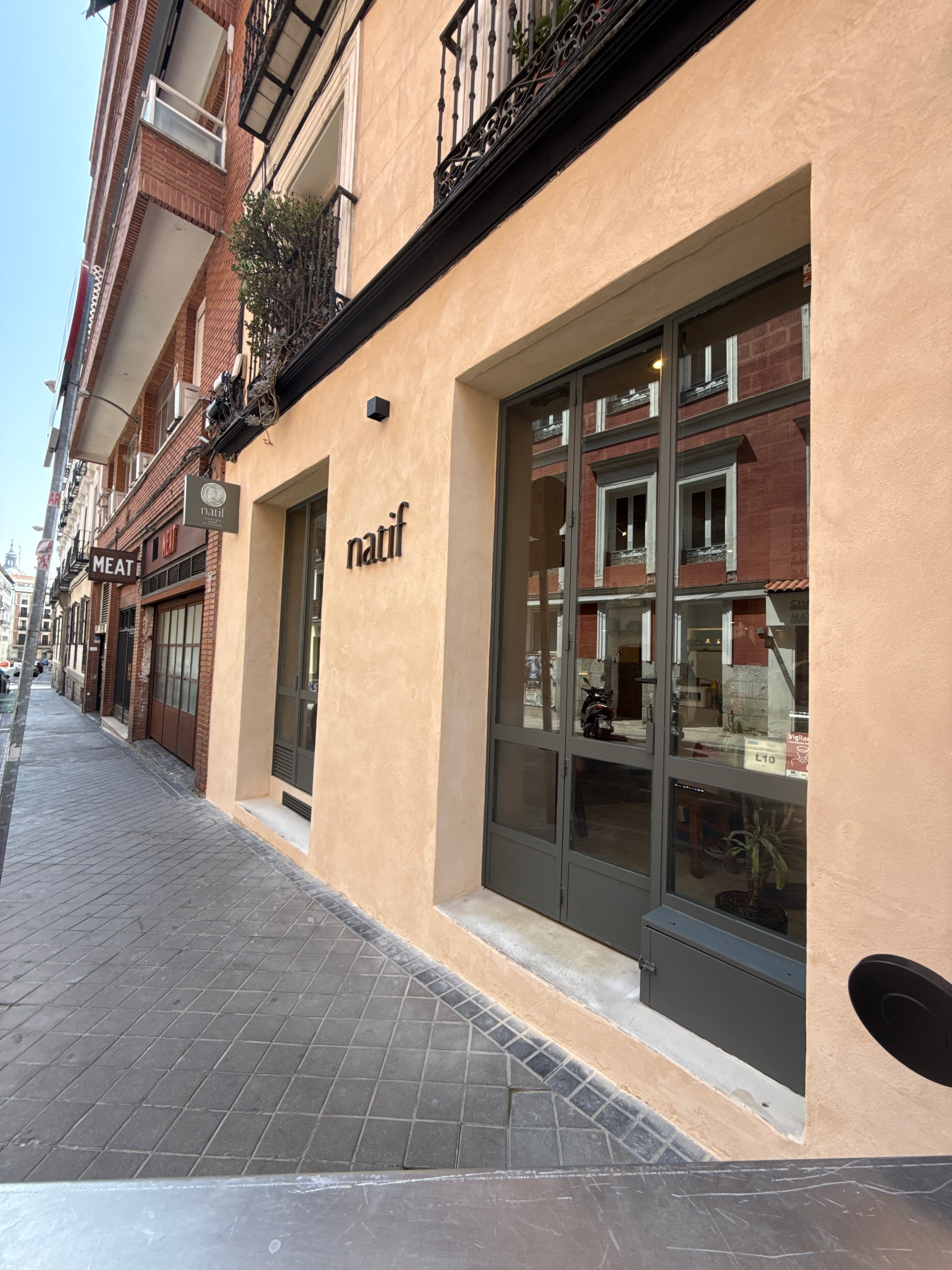 Fachada reformada de un local comercial en tonos tierra con grandes cristaleras y rótulo 'Natif', en una calle del centro de Madrid