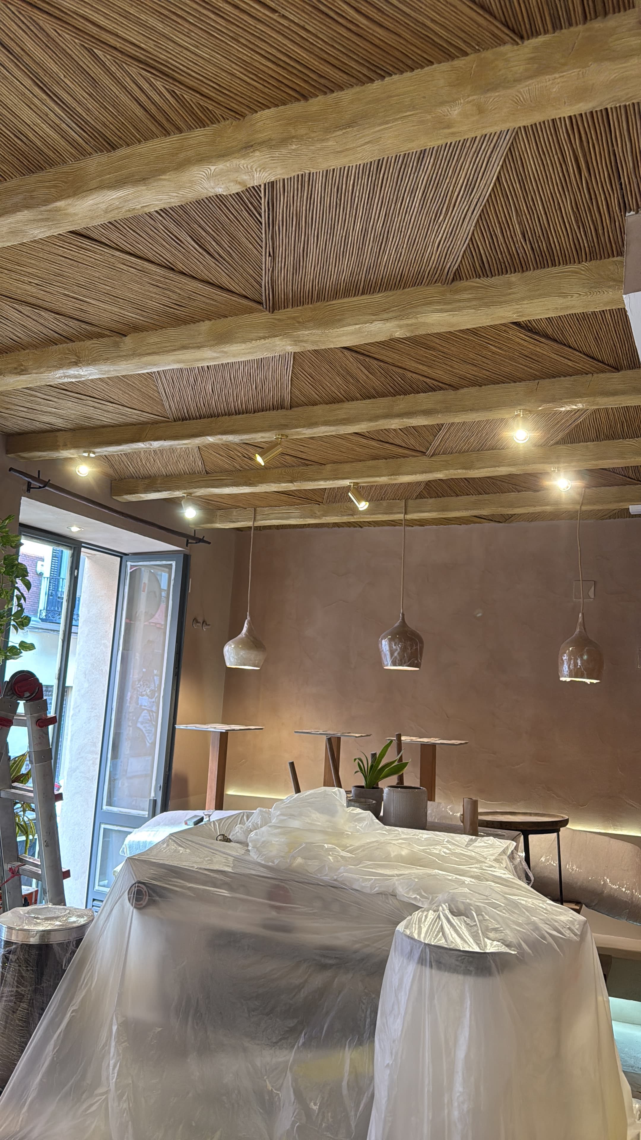 Interior de restaurante con techo revestido en caña trenzada, paredes en tono terracota y lámparas colgantes de cerámica artesanal