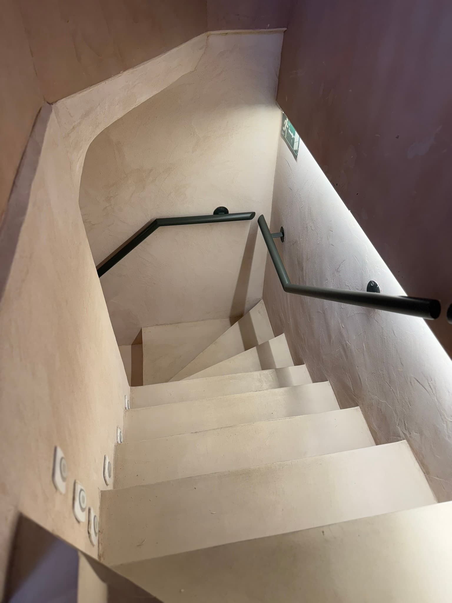Escalera interior con paredes curvas en estuco crema, pasamanos negro e iluminación indirecta integrada